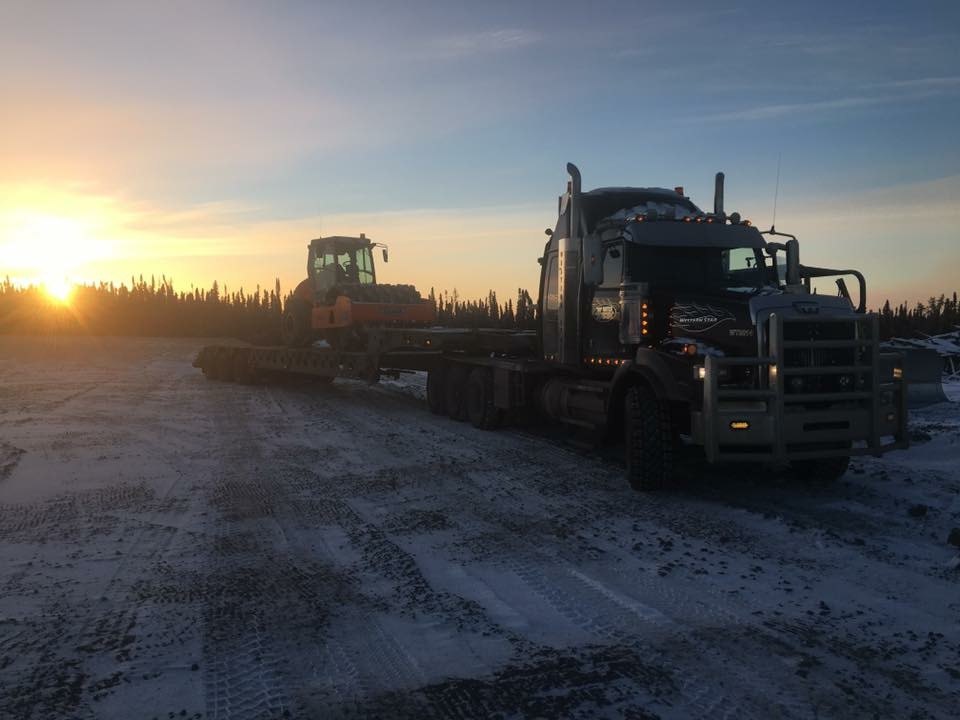 Lowbed truck hauling an excavator at sunrise